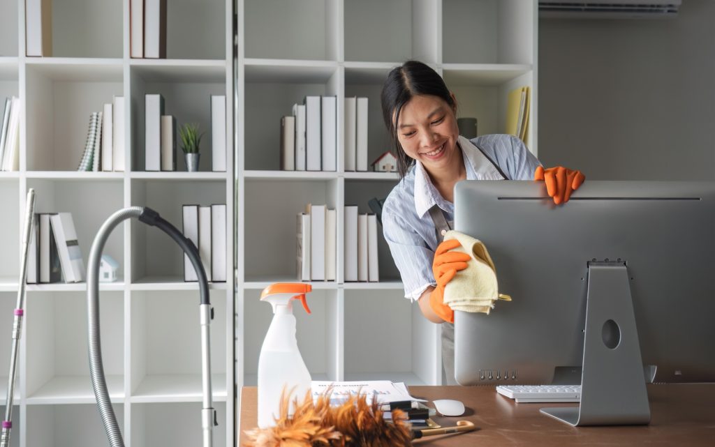 Young woman uses a cleaning cloth to disinfect the computer and equipment on the office table